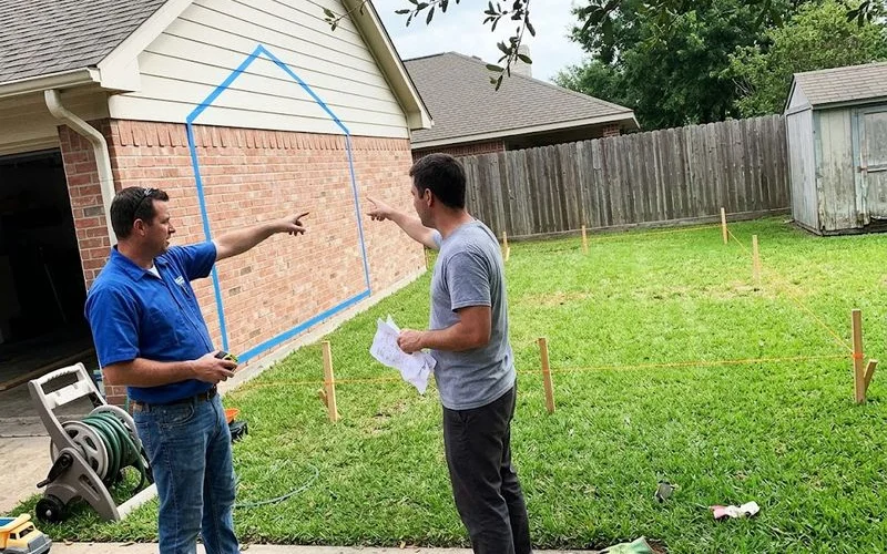 A homeowner and builder comparing site plans on a lot showing both an attached addition option and a detached garage footprint